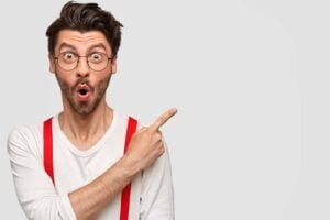 SGP Credit - Personal Loan With Low Interest Rate | Emotional bearded male has surprised facial expression, astonished look, dressed in white shirt with red braces, points with index finger at upper right corner, shows copy space for advertisement