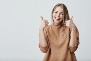 SGP Credit - Personal Loan With Low Interest Rate | Portrait of fair-haired beautiful female student or customer with broad smile, looking at the camera with happy expression, showing thumbs-up with both hands, achieving study goals. Body language