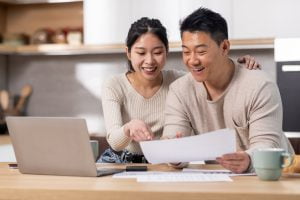 SGP Credit - Personal Loan With Low Interest Rate | Cheerful asian spouses paying bills on Internet, using laptop