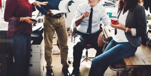 Four coworkers in a busy office gathered around a copier, discussing documents.