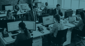 Open-plan office with coworkers at desks, some on phones and looking at computer screens.
