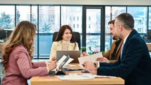 Team of four colleagues in a bright office, seated around a wooden table, reviewing documents and a laptop during a meeting.