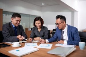 Three professionals in business attire collaborate at a conference table, reviewing documents and charts together.