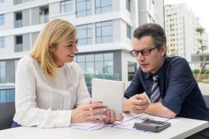 Two professionals reviewing a tablet outdoors at a modern office complex.
